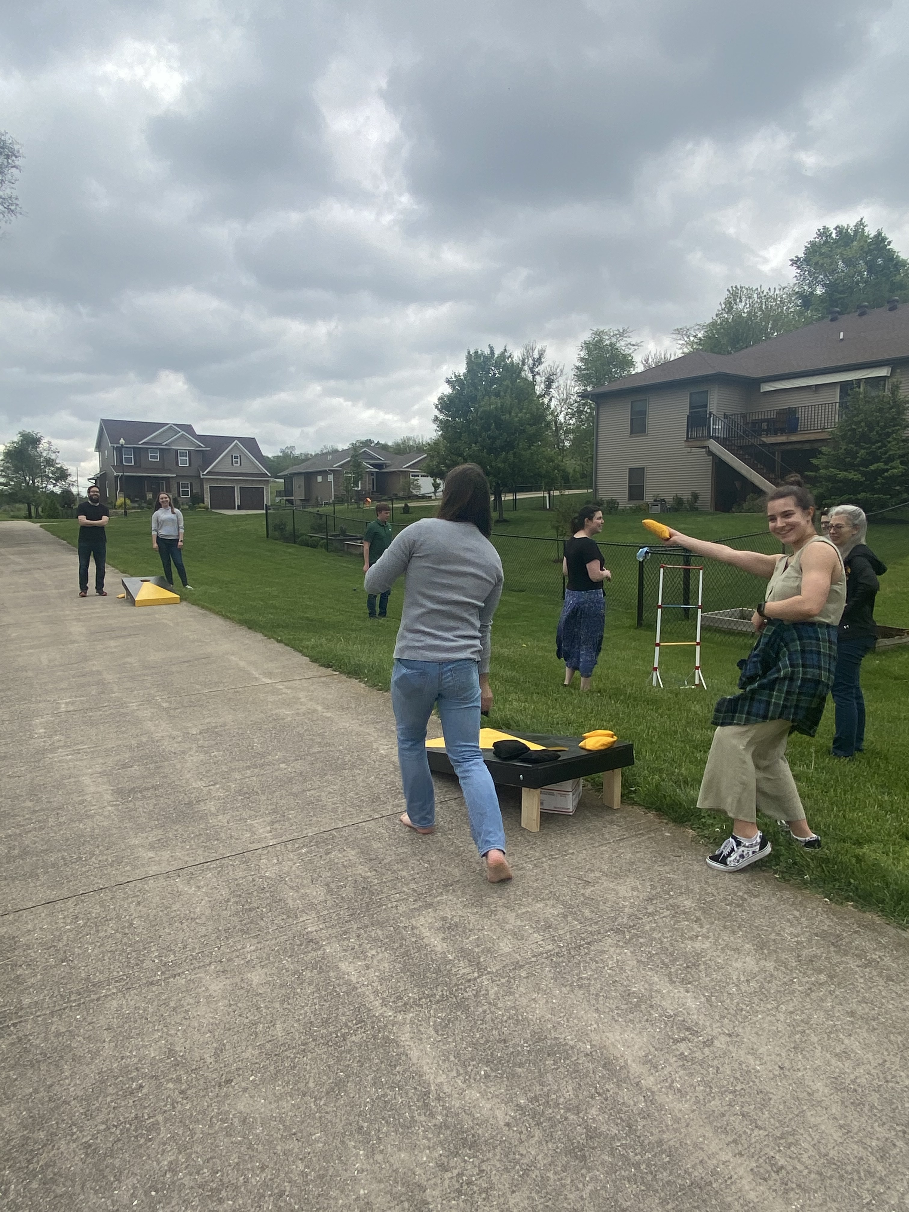 Leslie showing off her corn hole skills as she smiles at the camera. You can see other Cole group members playing yard games in the background