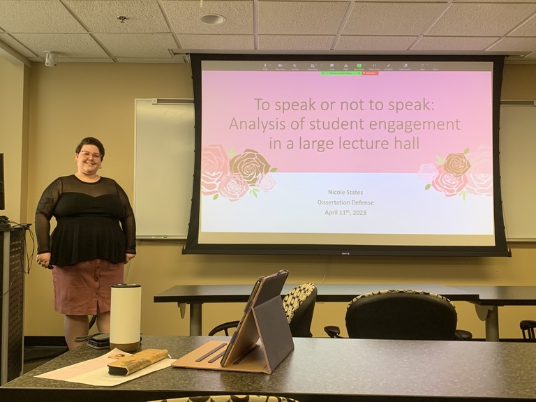 Nicole standing by her dissertation defense slides