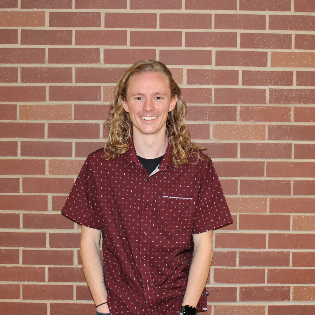 Andrew smiling standing in front of a brick wall