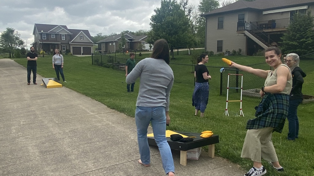 Leslie showing off her corn hole skills as she smiles at the camera. You can see other Cole group members playing yard games in the background